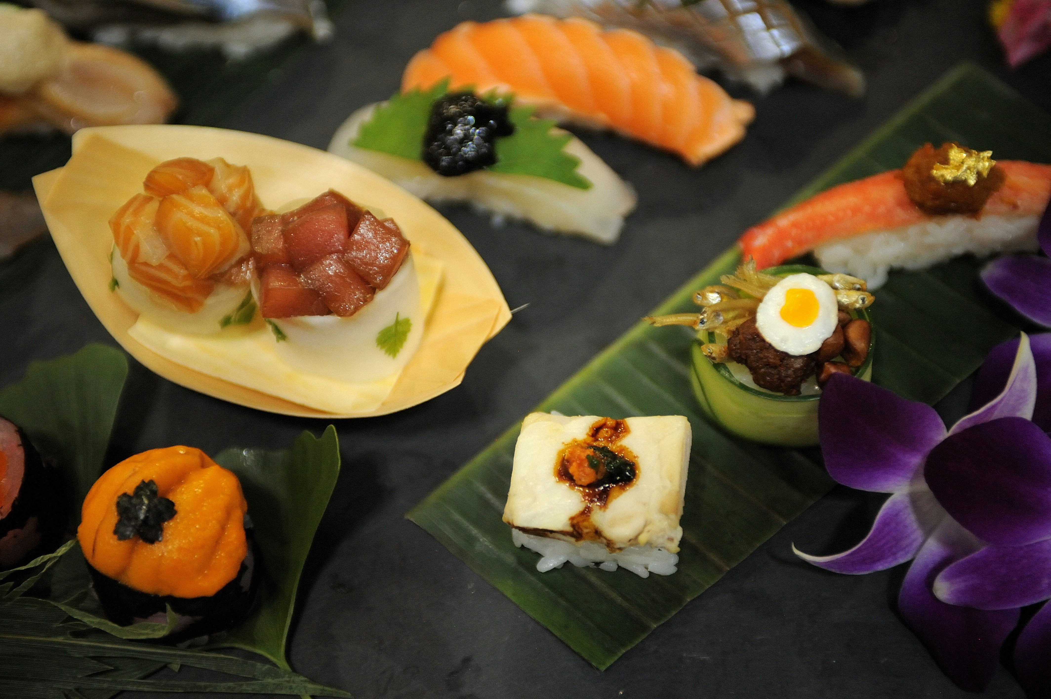 Ornate arrangements of sushi and small plates are arranged on leaves and in bamboo containers